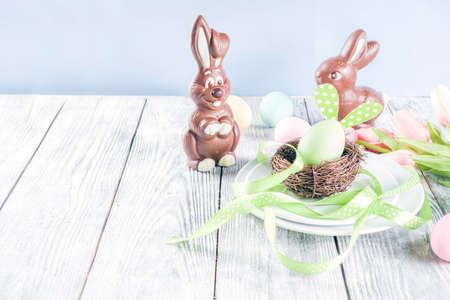 Easter holiday table setting with rabbits and eggs, plates with colorful eggs and chocolate bunny...