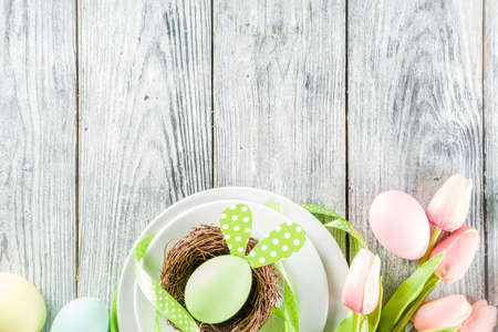 Easter holiday table setting with rabbits and eggs, plates with colorful eggs and chocolate bunny rabbits, festive ribbon, wooden background top view copy spaceの写真素材