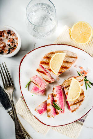 Grilled tuna fish steaks with lemon and spices, on portioned plate, white marble background copy space top viewの写真素材