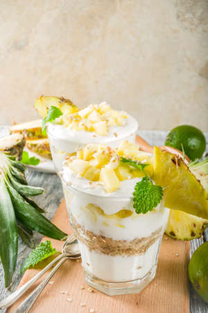 Pineapple breakfast layered parfait with Greek yogurt, homemade granola, pineapple slices, mint, wooden background,の写真素材