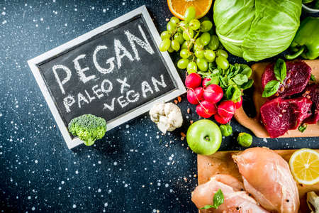 Trendy pegan diet - vegan plus paleo diet food concept, many fresh vegetables, fruits, raw beef and chicken meat, salmon fish, dark blue background top view copy spaceの写真素材