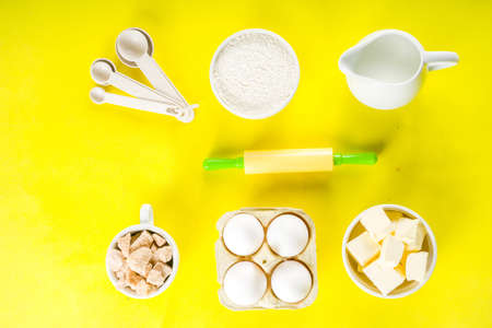 Baking ingredients and tools on trendy bright yellow background - flour, eggs, sugar, milk, butter, layout, flatlay top view copy spaceの写真素材