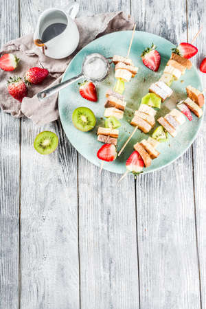 Summer breakfast snack. Fruit vegan dessert kebabs on skewers with toast French fried bread, fruits and berries. With powdered sugar and chocolate sauce.の写真素材