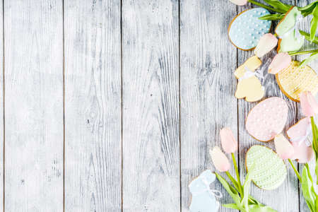Easter greeting card background with pastel colored eggs and homemade cookies shaped in eggs and bunnies rabbits. With a basket, tulips, rustic wooden table, copy space top view bannerの写真素材