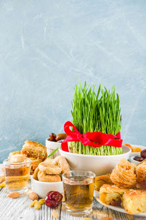 Happy Nowruz holiday background. Celebrating Nowruz sweets and treats- baklava, various dried fruits,  nuts, seeds, wooden background with green grass, copy spaceの写真素材