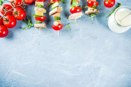 Healthy summer snack idea, salad sandwiches kebab on skewers, with bread slices, tomato, greens, cucumber, cheese, sausages, with yoghurt dipping, on light concrete background copy space top viewの写真素材