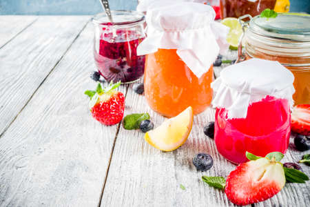 Assortment of various seasonal berry and fruit jams in jars on wooden table. Copy space