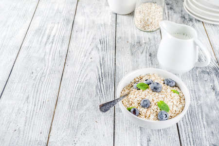 Healthy cereal and milk breakfast concept, dry oats in small bowl, with milk and fresh blueberry, white  wooden concrete background copy spaceの写真素材