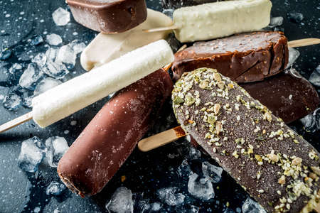 Assortment of various ice cream, vanilla and chocolate, with nuts, on a dark concrete background...