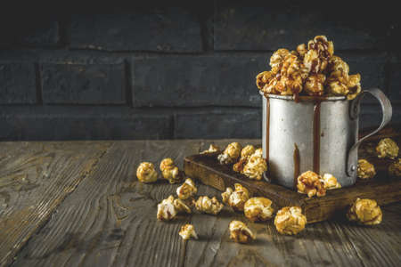 Homemade sweet caramel pop corn, with caramel topping, dark rustic background copy space