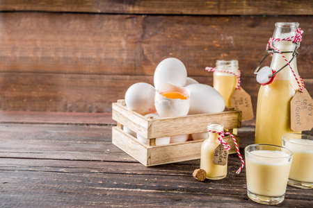 Traditional Italian Vov eggs liquor. German Egg Liqueur Eierlikor. In different bottle and shot glasses, Wooden background copy spaceの写真素材