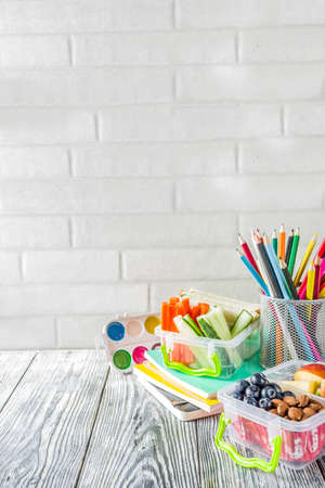 Healthy school lunch box. Kid's lunch box with sandwiches, fruit, vegetables, nuts, water and school supplies, White wooden backgroundの写真素材