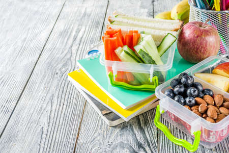 Healthy school lunch box. Kid's lunch box with sandwiches, fruit, vegetables, nuts, water and school supplies, White wooden backgroundの写真素材