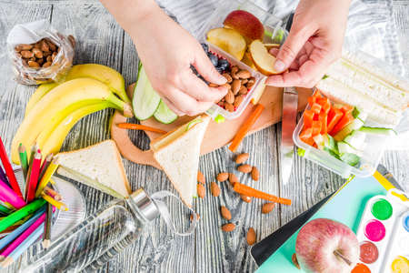 Mother cooking school lunch box set, Preparing healthy snacks - cheese sandwich with cucumber, carrot. nuts, fruits and vegetable in box. の写真素材