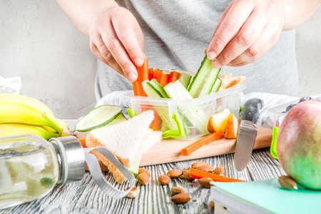 Mother cooking school lunch box set, Preparing healthy snacks - cheese sandwich with cucumber, carrot. nuts, fruits and vegetable in box. の写真素材