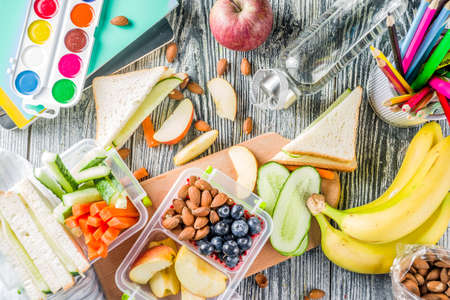 Healthy school lunch box. Kid's lunch box with sandwiches, fruit, vegetables, nuts, water and school supplies, White wooden backgroundの写真素材