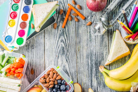 Healthy school lunch box. Kid's lunch box with sandwiches, fruit, vegetables, nuts, water and school supplies, White wooden backgroundの写真素材