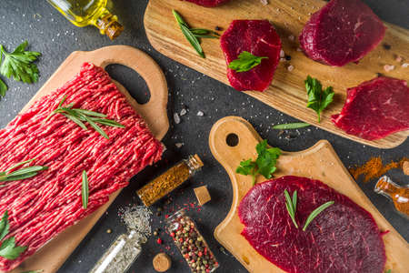 Different raw steak and minced beef meat with herbs and spices for cooking, black concrete or stone tableの写真素材