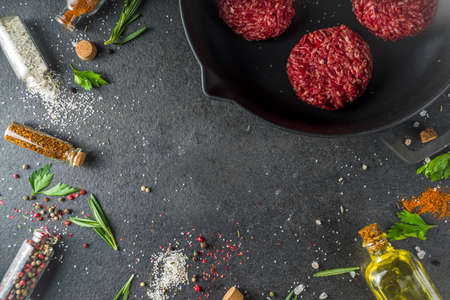 Raw minced meat beef burger cutlets. Cooking meat and burgers background with olive oil. herb, spices, black stone or concrete table, above, copy spaceの写真素材
