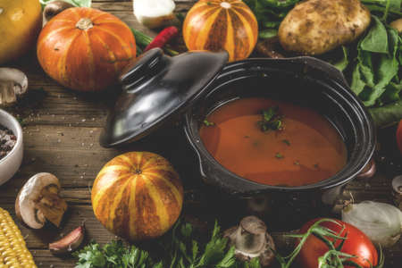 Autumn seasonal cooking concept. Various autumn vegetables (pumpkin,carrot,paprika,tomatoes,ginger) with pot for cooking soup. wooden background の写真素材
