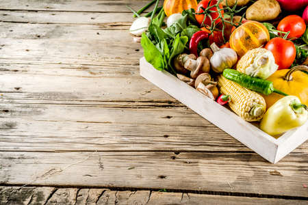 Autumn food concept. Healthy organic harvest vegetables and ingredients pumpkin, greens, tomatoes, corn, wooden kitchen table background. Thanksgiving seasonal cooking ingredients.の写真素材