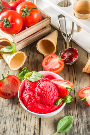Vegetable gelato. Tomato ice cream with fresh tomatoes and basil and leaves, old rustic wooden background. の写真素材
