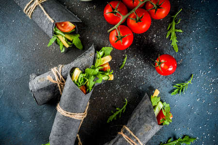 Trendy healthy vegan food. Black charcoal wrapped sandwiches, with fresh vegetables, cheese, on a dark blue background, space for textの写真素材