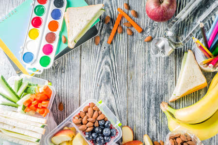 Healthy school lunch box. Kid's lunch box with sandwiches, fruit, vegetables, nuts, water and school supplies, White wooden backgroundの写真素材