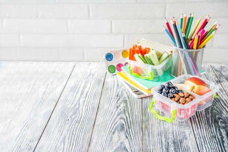 Healthy school lunch box. Kid's lunch box with sandwiches, fruit, vegetables, nuts, water and school supplies, White wooden backgroundの写真素材