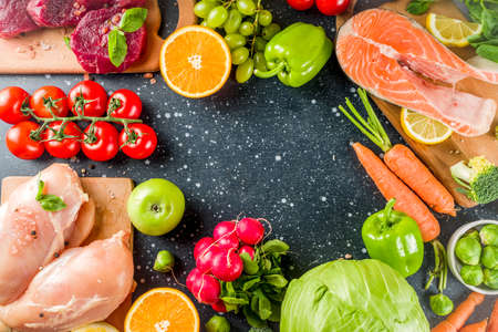 Trendy pegan diet - vegan plus paleo diet food concept, many fresh vegetables, fruits, raw beef and chicken meat, salmon fish, dark blue background top view copy spaceの写真素材