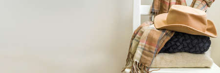Autumnal cozy mood concept. Home interior, warm clothes, sweater, plaid, scarf, hat with autumn...