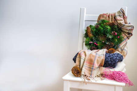 Christmas preparations, new year concept. Home decoration. Domestic interior, warm clothes sweater, plaid, scarf, Christmas tree wreath, with cones, berries. White wall, with chair, marshmallow cupの写真素材
