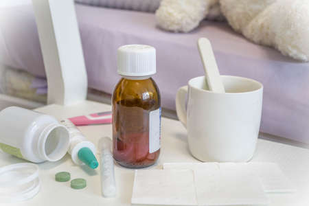 Seasonal flu concept, ill kid girl with with pills, medicines, thermometer. In the children's room in bed, with plush toys copy spaceの写真素材