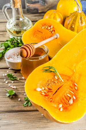 Halves of raw pumpkin butternut squash, with olive oil, spices and ingredients for cooking on rustic old wooden background.Top view copy space.の写真素材