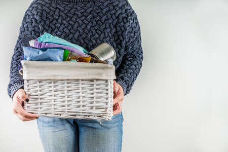 Giving and helping concept. Reuse and recycling theme. Woman holds and folds donation box with clothes, children's toys, food. On a white background, Girl's hands in pictureの写真素材