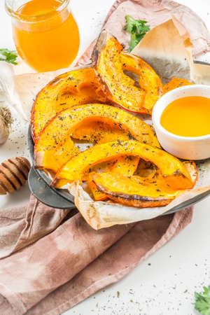 Autumn vegetarian food recipe. Organic roasted vegetables, Baked fried Hokkaido pumpkin with olive oil, herbs, garlic and honey. On a white stone background, copy spaceの写真素材