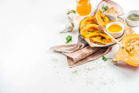 Autumn vegetarian food recipe. Organic roasted vegetables, Baked fried Hokkaido pumpkin with olive oil, herbs, garlic and honey. On a white stone background, copy spaceの写真素材