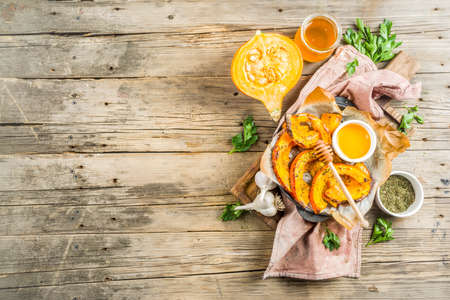 Autumn vegetarian food recipe. Organic roasted vegetables, Baked fried Hokkaido pumpkin with olive oil, herbs, garlic and honey. On wooden rustic background, copy spaceの写真素材