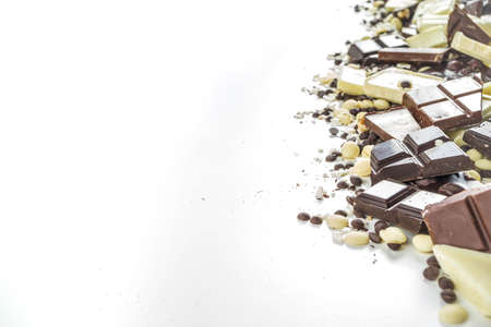 Assorted different types of chocolate. Broken pieces of dark, milk and white chocolate, with nuts, cooking chocolate, shavings. On a black stone concrete background, top view copy spaceの写真素材