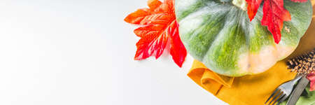 Autumn cutlery background. Fall card background for menu or invitation, banner format. With fork, knife, napkins, pumpkin, plate, multicolored leaves. On white table, top view copy spaceの写真素材