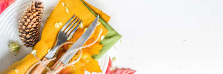 Autumn cutlery background. Fall card background for menu or invitation, banner format. With fork, knife, napkins, pumpkin, plate, multicolored leaves. On white table, top view copy spaceの写真素材