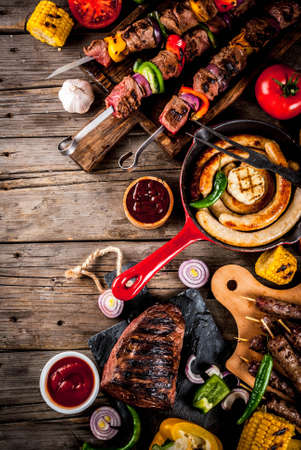 Assortment various barbecue food grill meat, bbq party fest - shish kebab, sausages, grilled meat fillet, fresh vegetables, sauces, spices, on old wooden rustic table, above copy spaceの写真素材