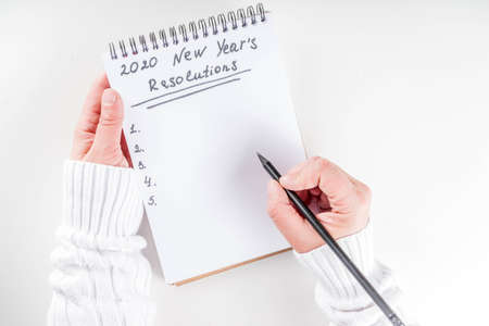 Woman hands ready to write list of her 2020 new year goals in notepad, top view flatlay copy space...