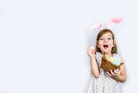 Happy cute child girl in rabbit costume with bunny ears holds basket painted eggs in hands.