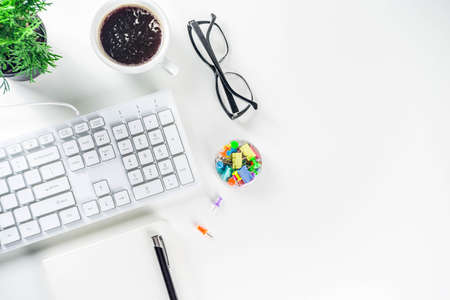 Office creative desk with supplies and coffee cup. White office table with keyboard, blank notebook, glasses, supplies and coffee cup. Flatlay layout copy space top view