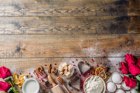 Valentine day baking background. Ingredients for cooking Valentine's heart cookies. Flour, eggs, sugar, spices on wooden background with red flower roses. Top view copy space.の写真素材