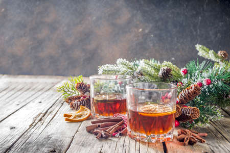 Christmas winter alcohol drink. Orange, spice and bourbon whiskey alcoholic cocktail in two glasses, wooden background with christmas tree branches and decor, copy spaceの写真素材