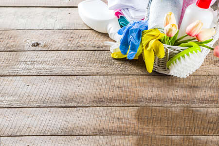 Spring home cleaning and housekeeping concept, Basket with cleaning items, utensils, supplies. Copy space over wooden background with spring blossom flowersの写真素材