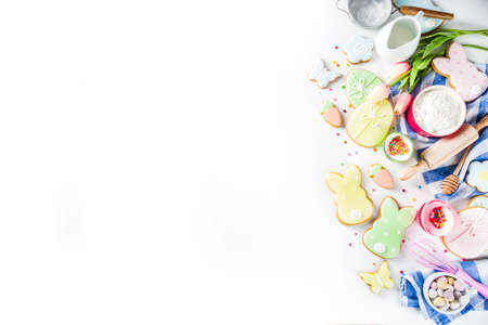 Sweet Easter baking cooking background with traditional Easter bunny and egg cookies, sugar sprinkles, ingredients, utensils. White table background copy space layoutの写真素材