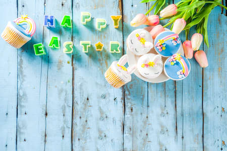 Easter holiday greeting card background. Cute homemade cupcakes with traditional Easter bunny, egg and springtime flowers decor. Happy easter concept. Copy space for your textの写真素材